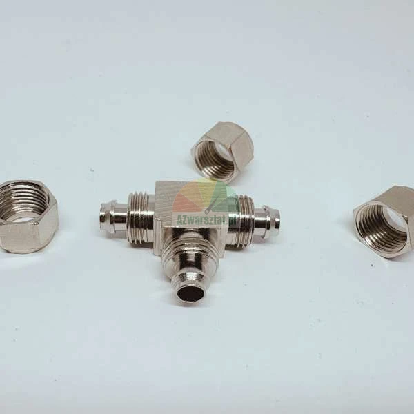 Metalowy trójnik hydrauliczny z trzema nakrętkami na białym tle.