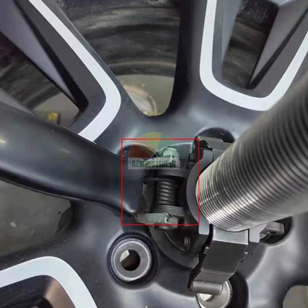 Zbliżenie na czarną felgę aluminiową zamontowaną na wyważarce z czerwonym kwadratem zaznaczającym mechanizm zacisku montażowego.